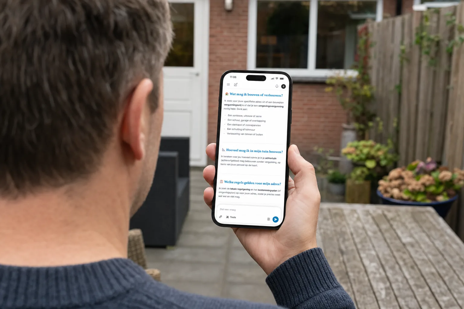 Huiseigenaar checkt in zijn tuin op zijn telefoon met Vergunnex of zijn bouwplan vergunningvrij is.